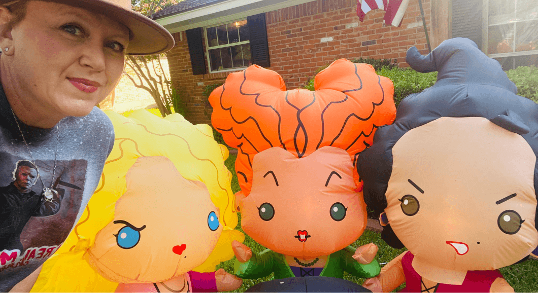 A woman stands in front of Hocus Pocus blow-up yard dolls.