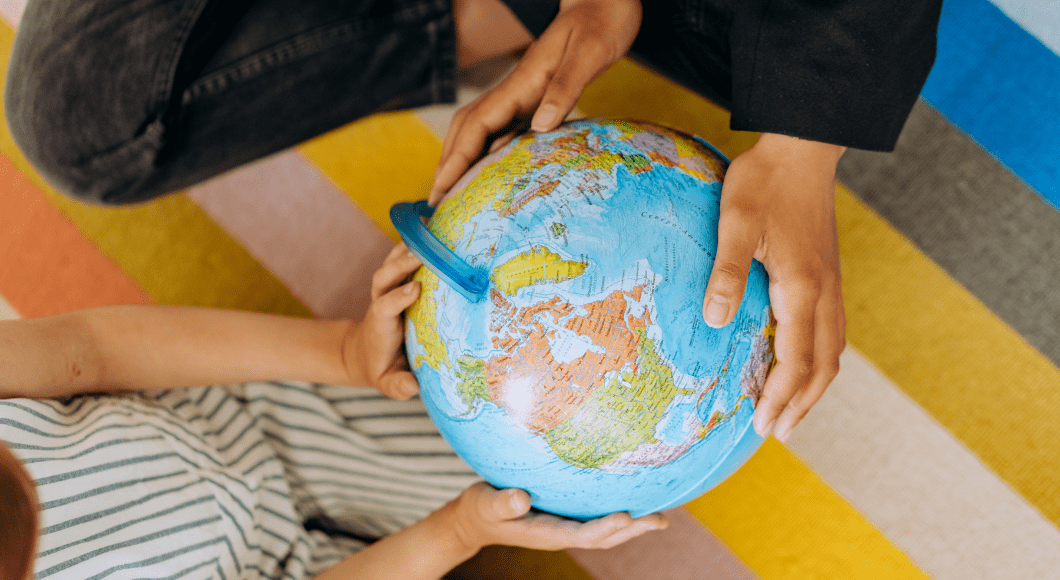 Adult hand and child's hand on globe.