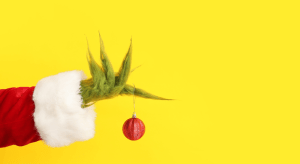 The Grinch's hand holding a red ornament with a yellow background