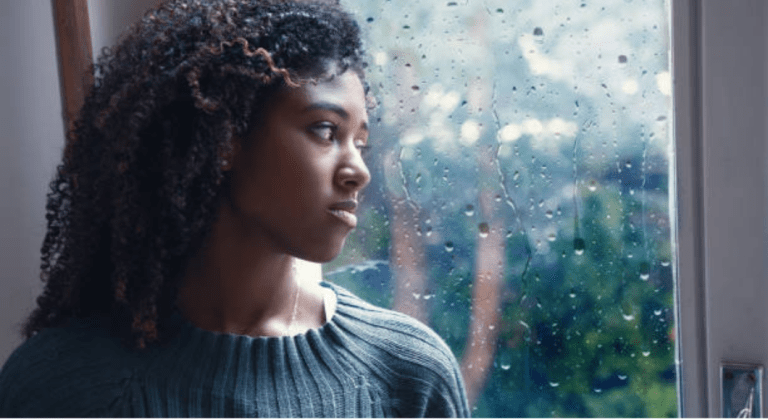 A sad woman looks out the window at a rainy day.