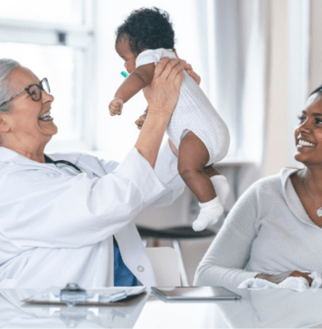 And older doctor holds a baby with the mother sitting nearby