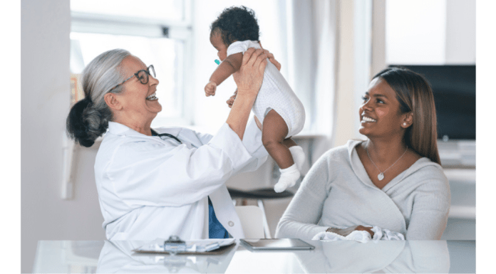 And older doctor holds a baby with the mother sitting nearby