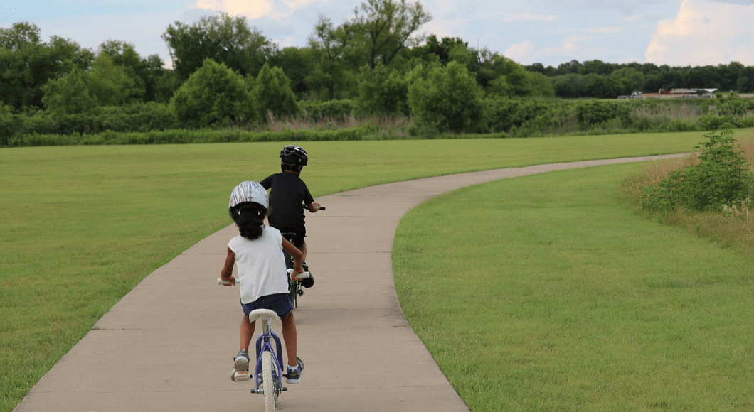 Two children ride bicycles on a paved path.
