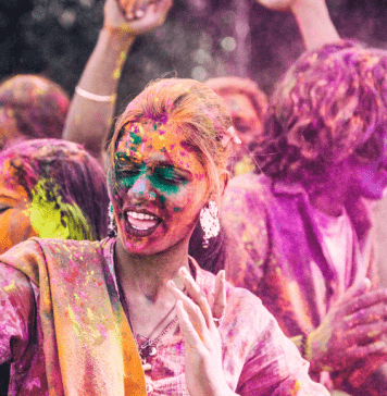 A woman covered in colored powder dances and sings at the Holi festival of colors.