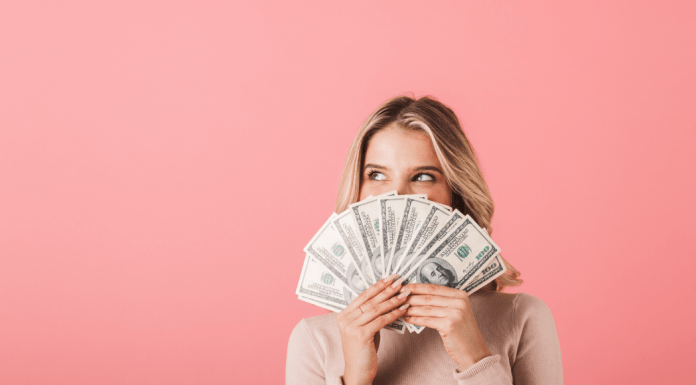 woman holds a fan of $100 bills in front of her face