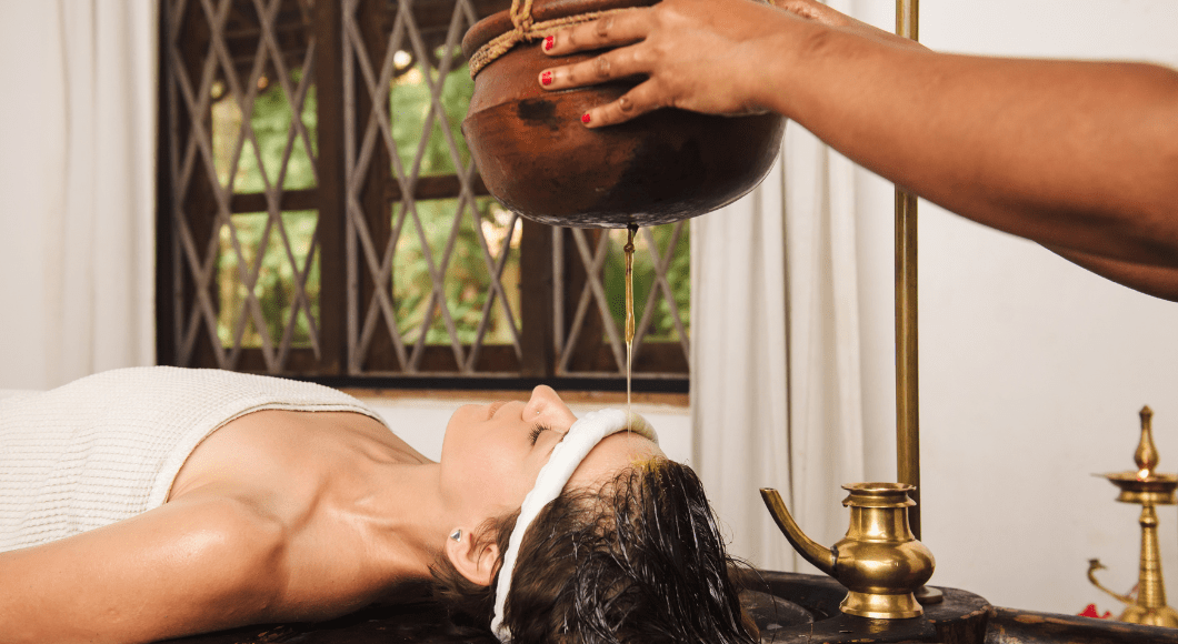 Massage therapist pours oil on a client's head for an ayurvedic spa treatment.