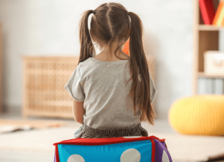 Little girl with piggy tails sits alone with her back to the camera.