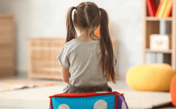 Little girl with piggy tails sits alone with her back to the camera.