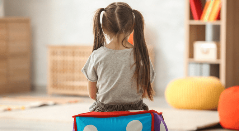 Little girl with piggy tails sits alone with her back to the camera.