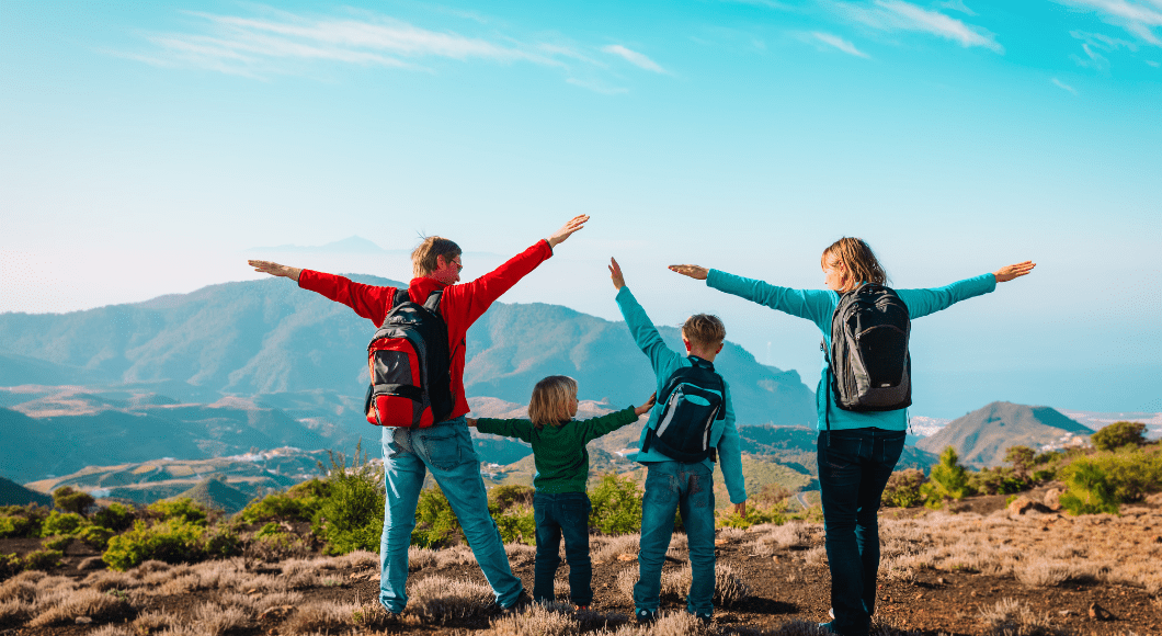 A family of four spread their arms like wings and carry travel packs.