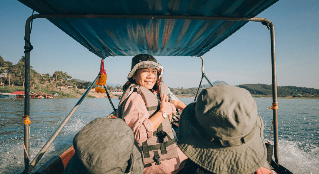 Two daughters look ahead at their mom looking back on them on a fishing boat in Southeast Asia.