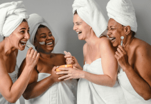 Women of different ethnicities laugh together at the spa wearing towels and hair wraps.
