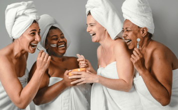 Women of different ethnicities laugh together at the spa wearing towels and hair wraps.