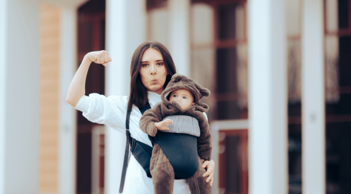 Strong mom wears her baby in a newborn carrier and makes a silly face