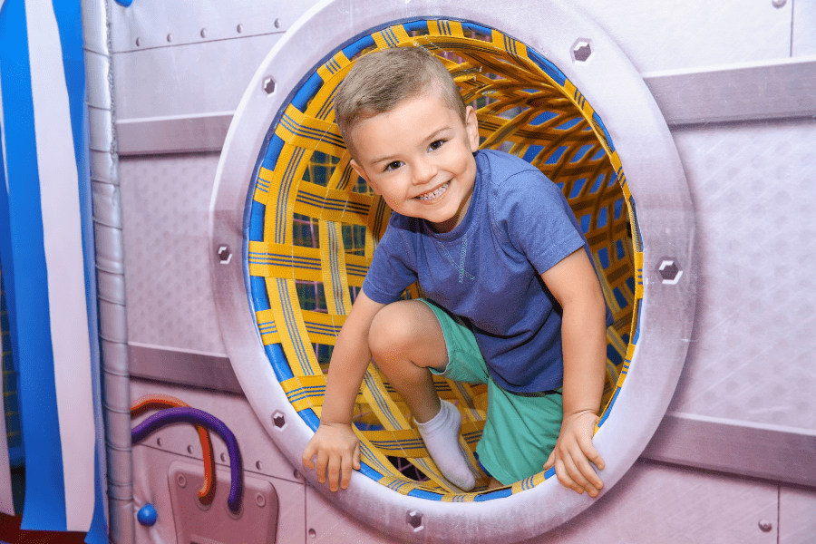 Toddler boy crawls through a tunnel at an indoor play facility.