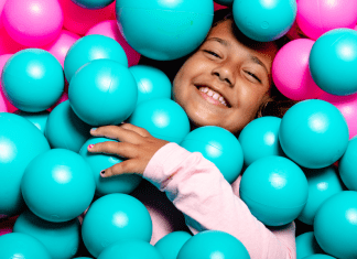 Big kid lays in ball pit smiling.