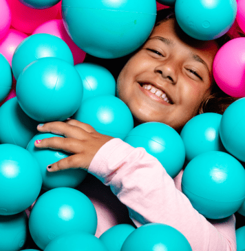 Big kid lays in ball pit smiling.