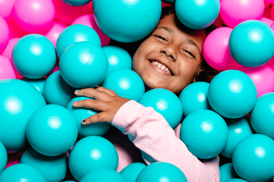 Big kid lays in ball pit smiling.