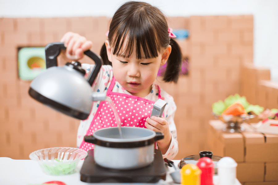 Little girl role plays house with a toy kettle and pan.