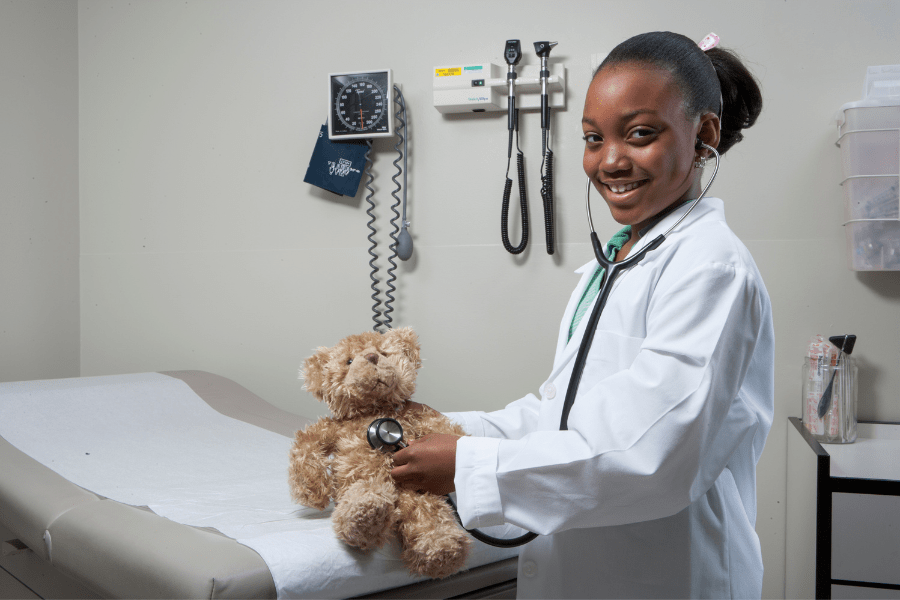 Little girl dresses up as a doctor and cares for a teddy bear in an indoor play facility.