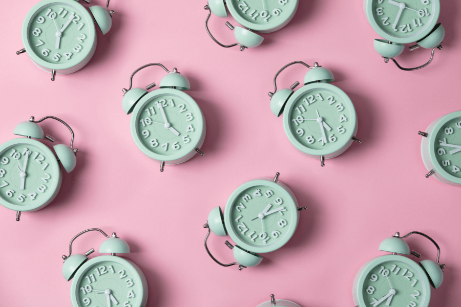 Green alarm clocks set to 5:00 and after on a pink background.