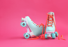 Pair of pastel blue roller skates with orange laces on a bright pink background.