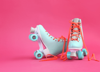 Pair of pastel blue roller skates with orange laces on a bright pink background.