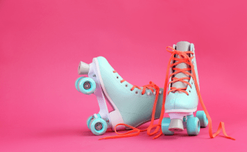 Pair of pastel blue roller skates with orange laces on a bright pink background.