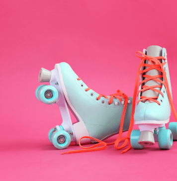 Pair of pastel blue roller skates with orange laces on a bright pink background.