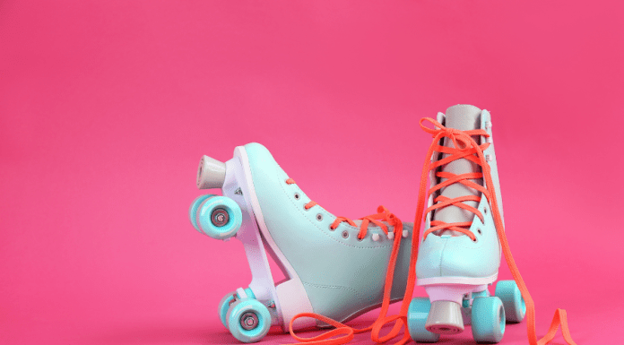 Pair of pastel blue roller skates with orange laces on a bright pink background.