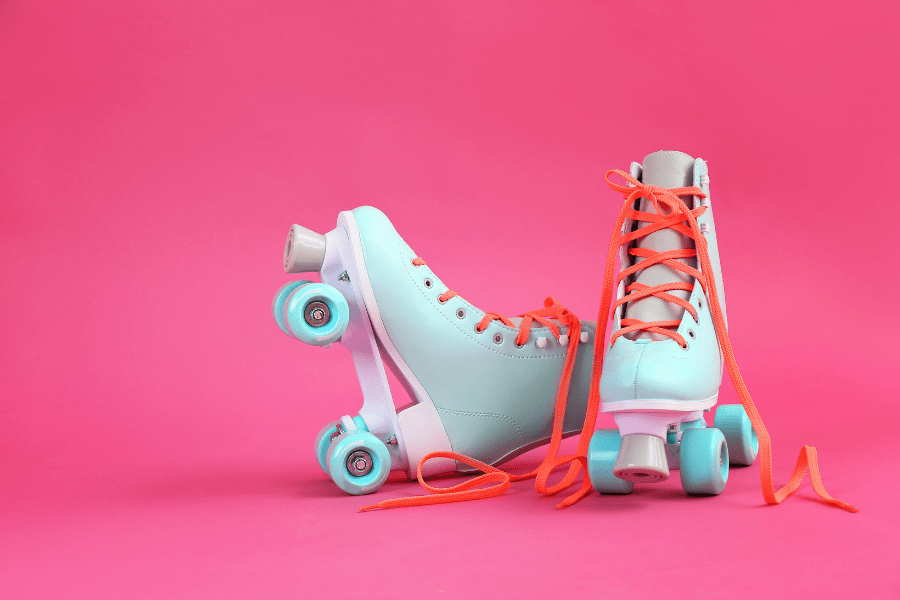 Pair of pastel blue roller skates for indoor skating with orange laces on a bright pink background.