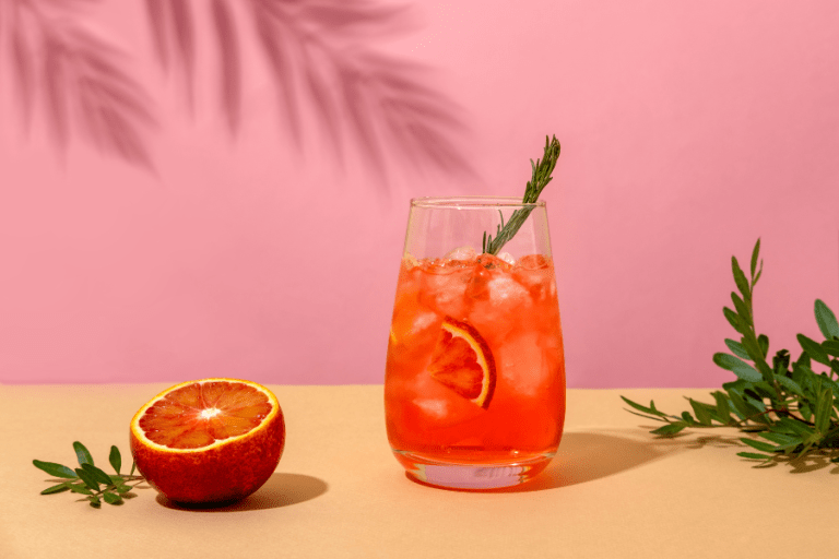 Negroni cocktail and a blood orange on a pink background