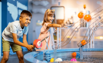 A boy and girl play with an interactive water machine inside a museum.