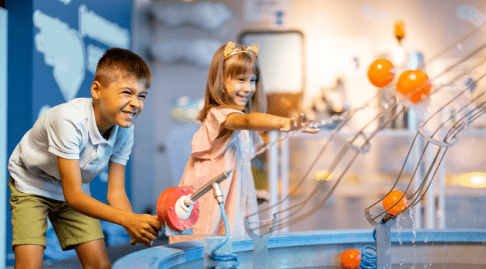 A boy and girl play with an interactive water machine inside a museum.