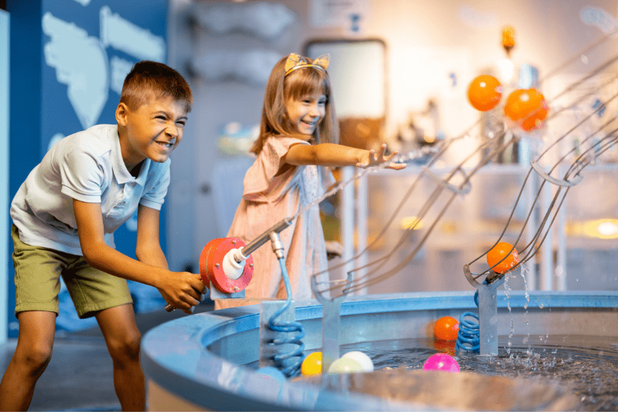 A boy and girl play with an interactive water machine inside a museum.