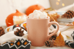 A mug of hot chocolate piled with marshmallows sits on a table with autumn decor.