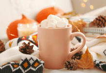 A mug of hot chocolate piled with marshmallows sits on a table with autumn decor.