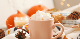 A mug of hot chocolate piled with marshmallows sits on a table with autumn decor.