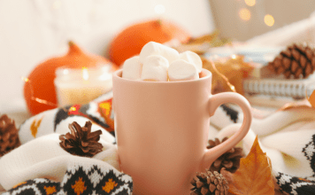 A mug of hot chocolate piled with marshmallows sits on a table with autumn decor.