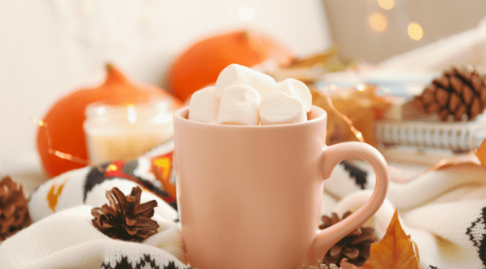 A mug of hot chocolate piled with marshmallows sits on a table with autumn decor.